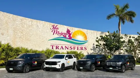 Four SUVs in front of the Isla Mujeres Transfers logo on a stone wall